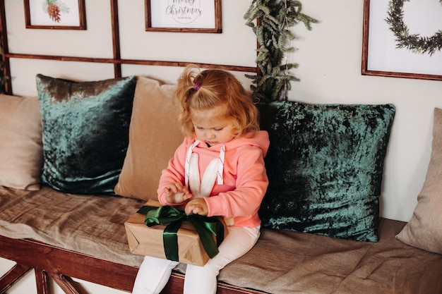小さなかわいい女の子シスのウェーブのかかった髪がソファに座ってプレゼントの入った箱を開ける