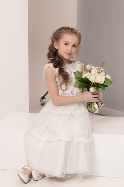 Little pretty girl with flowers dressed in wedding dresses