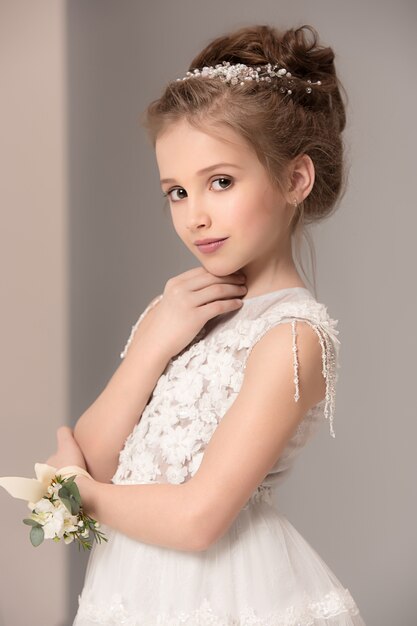 Little pretty girl with flowers dressed in wedding dresses