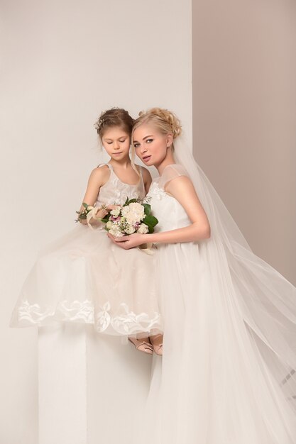 Little pretty girls with flowers dressed in wedding dresses