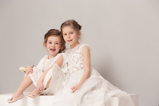 Little pretty girls with flowers dressed in wedding dresses.