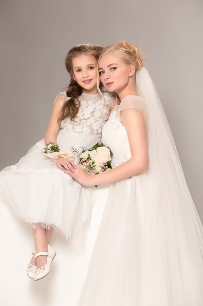 Little pretty girls with flowers dressed in wedding dresses