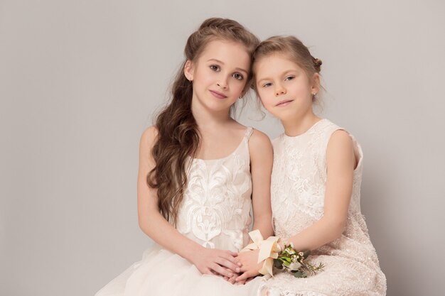 Little pretty girls with flowers dressed in wedding dresses