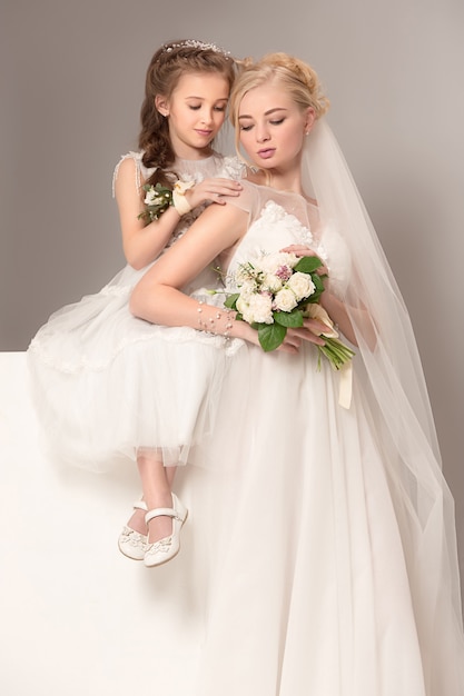 Little pretty girls with flowers dressed in wedding dresses