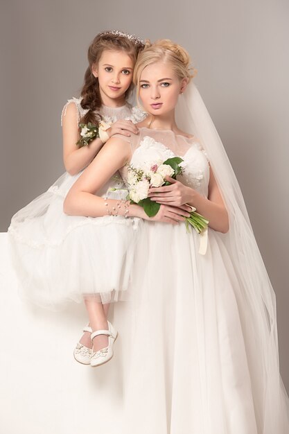 Little pretty girls with flowers dressed in wedding dresses