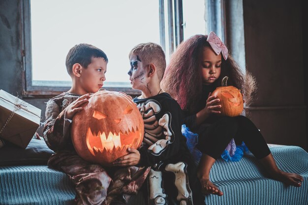 Маленькие симпатичные детишки готовы к Хэллоуину, они держат в руках резные тыквы.