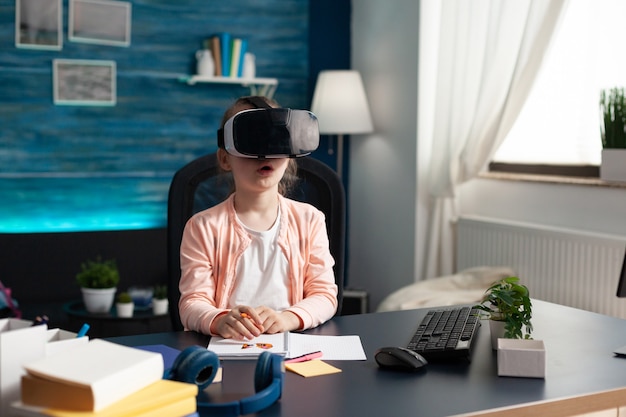 Little pupil at home desk using vr glasses for class