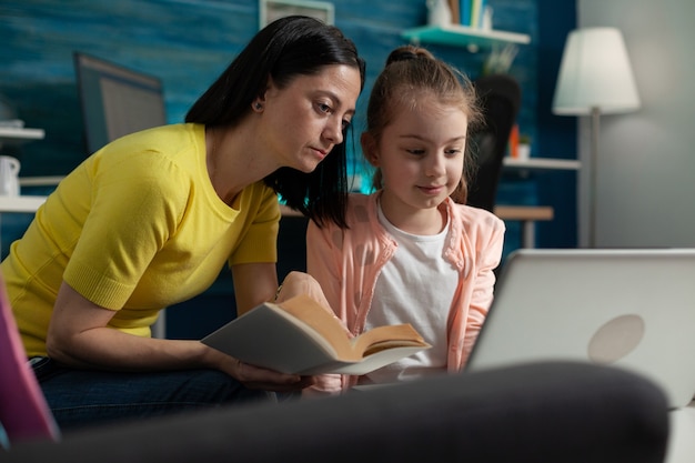 Little pupil using laptop for homework and mom assisting