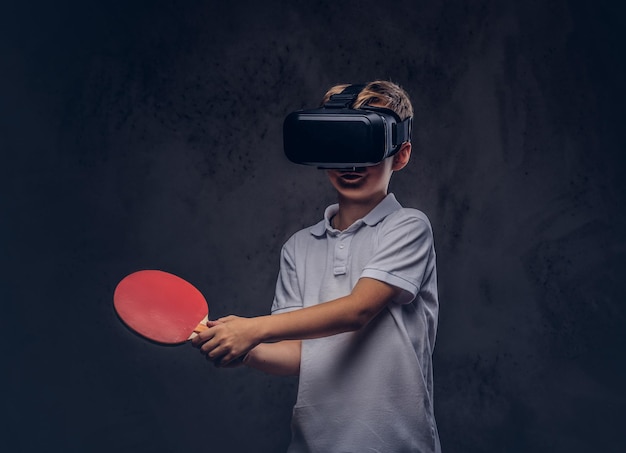 Free photo little redhead boy dressed in a white t-shirt playing ping-pong with a virtual reality glasses. isolated on a dark textured background.