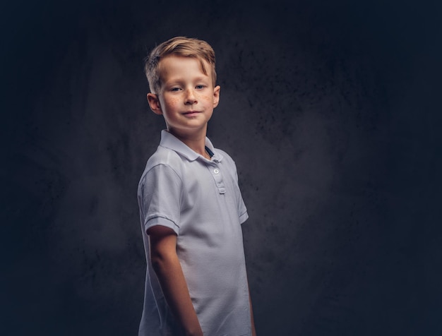 Free photo little redhead boy dressed in a white t-shirt posing in a studio. isolated on a dark textured background.