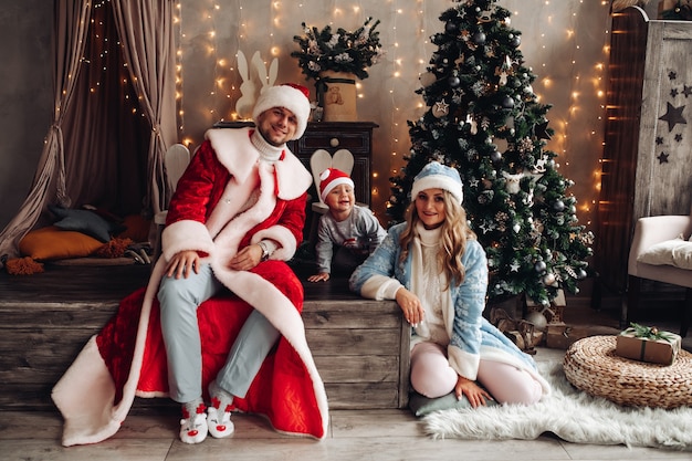 Little Santa, Father Frost and Snow Maiden smiling in xmas interior with decorated Christmas tree.