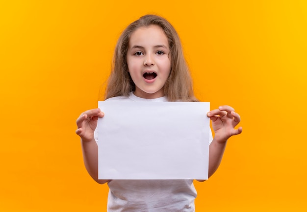 Free photo little school girl wearing white t-shirt holding paper on isolated orange wall