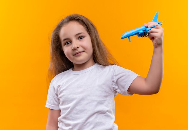 孤立したオレンジ色の壁におもちゃの計画で遊ぶ白いTシャツを着て小さな女子高生