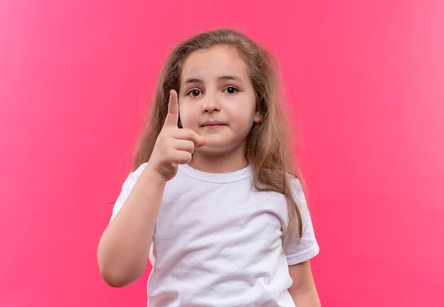 白いTシャツを着ている小さな女子高生は、孤立したピンクの壁の上を指しています