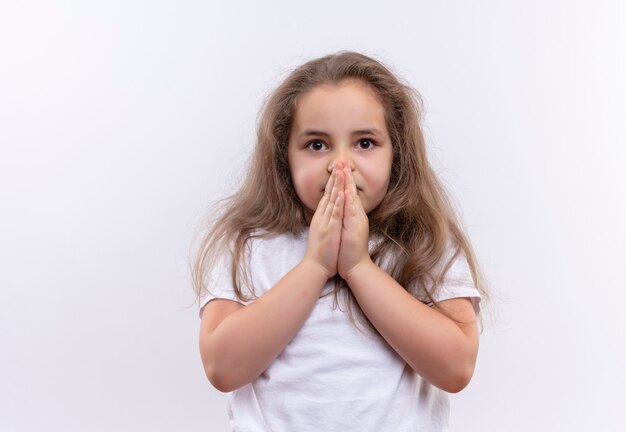 little school girl wearing white t-shirt showing pray gesture on isolated white wall