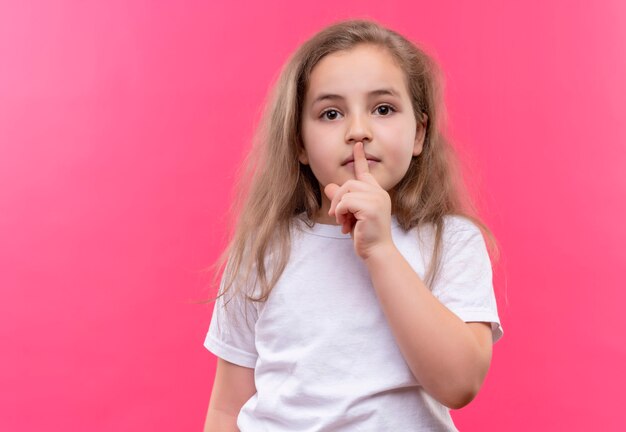 Free photo little school girl wearing white t-shirt showing silence gesture on isolated pink wall