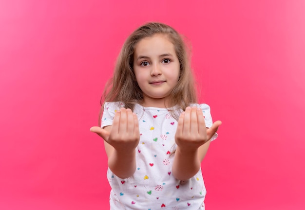 Foto gratuita piccola ragazza della scuola che indossa la maglietta bianca che mostra le dimensioni sul muro rosa isolato