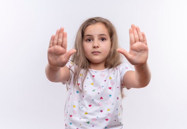 孤立した白い壁に停止ジェスチャーを示す白いTシャツを着ている小さな女子高生