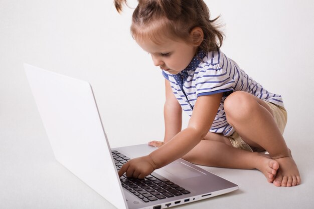 Little small female kid sits in front of opened laptop