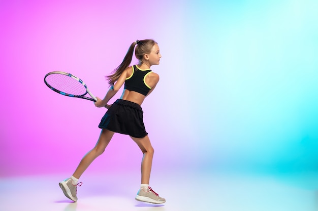 Little tennis girl in black sportwear isolated on gradient wall in neon light