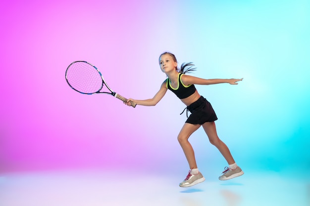 Little tennis girl in black sportwear isolated on gradient wall in neon light