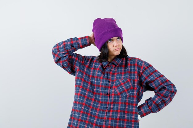 Free photo little woman beanie keeping hand on hip while holding hand on head looking thoughtful