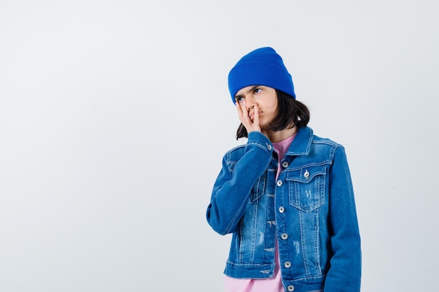 Free photo little woman holding hand on cheek in t-shirt and denim jacket looking wistful