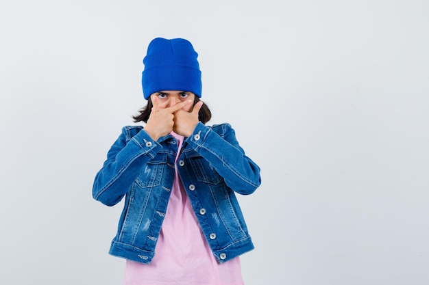 Piccola donna che tiene pistole a mano sulla bocca in maglietta e giacca di jeans che sembra seria