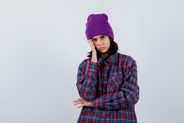 Free photo little woman holding hand on head in checkered shirt and beanie looking thoughtful