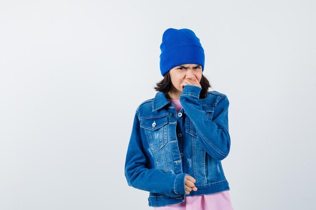 Little woman holding hand on mouth in t-shirt denim jacket beanie looking wistful