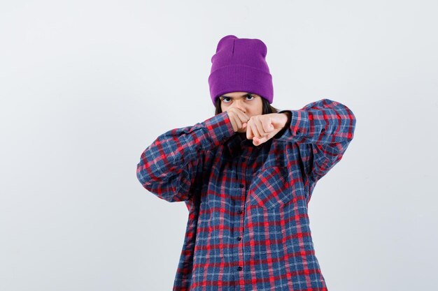 Little woman sting in fight pose in checkered shirt and beanie looking spiteful