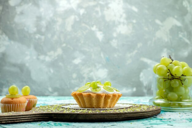 little yummy cake with delicious cream and sliced and fresh grapes cookies on blue light desk, cake sweet fruit