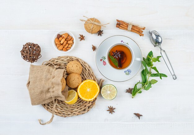 Llimes and cookies on round placemat with a cup of tea,a bowl of almonds and a tea strainer