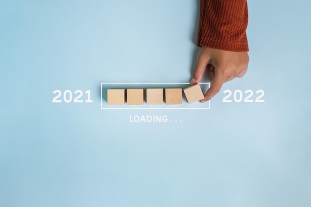 Loading new year 2021 to 2022 with hand putting wood cube in progress bar over blue background