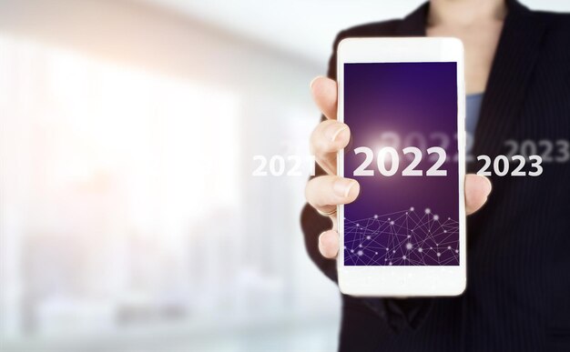 Loading year 2021 to 2022. start concept. hand hold white smartphone with digital hologram 2022 sign on light blurred background. happy new year 2022 -