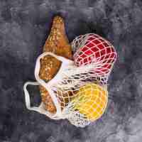 Free photo loaf of bread; red and yellow bell pepper in white net bag on textured backdrop