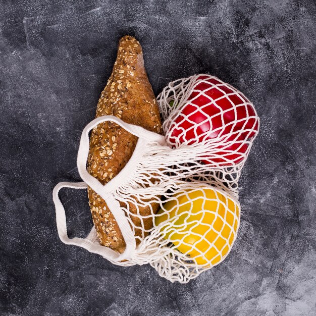 Loaf of bread; red and yellow bell pepper in white net bag on textured backdrop