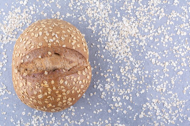 Loaf of bread sitting in a scattered mess of flakes on marble surface