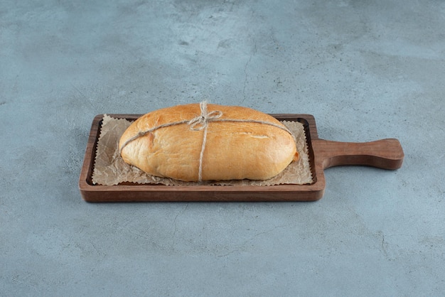 Буханка хлеба, перевязанная веревкой на деревянной доске.
