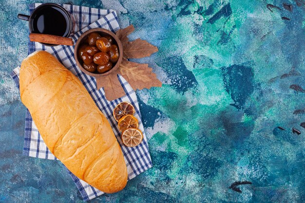 Loaf of bread with cup of tea and berry jam on blue surface.