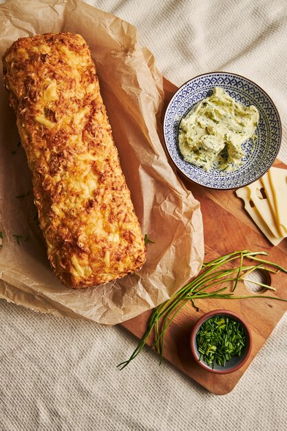 Loaf of cheese bread with herbal butter on a wooden plate with herbs