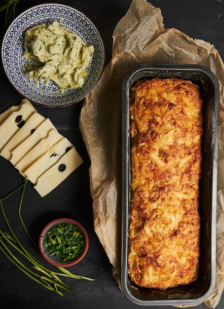 Loaf of cheese bread with herbal butter on a wooden plate with herbs