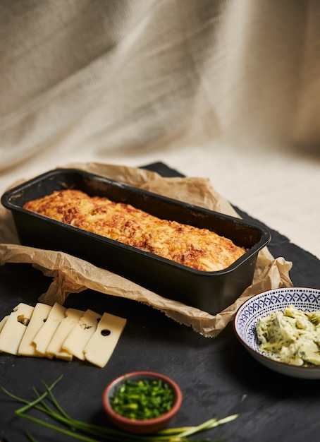 Loaf of cheese bread with herbal butter on a wooden plate with herbs