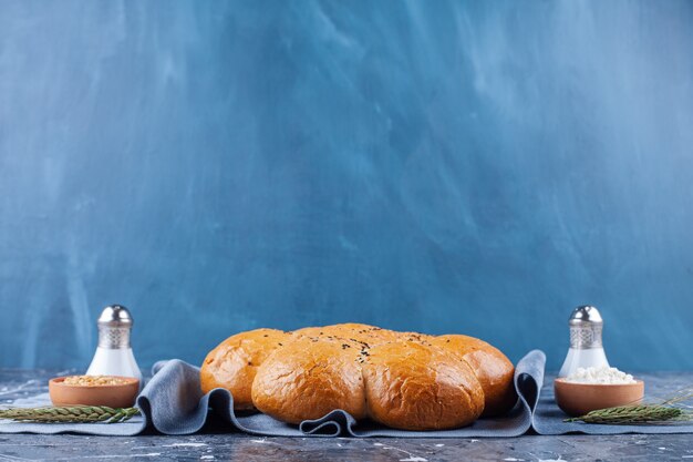 Loaf of fresh fragrant bread with salt and pepper on blue.