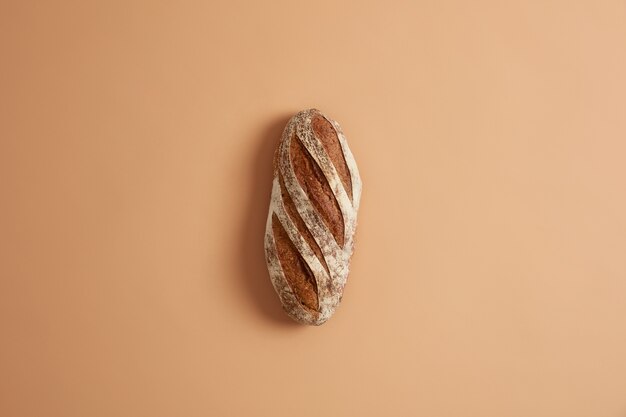 Loaf of fresh homemade crisp french whole grain bread prepared from organic flour, made on leaven, isolated on brown studio background. Bakery and food concept. Home cooking and food preparation.