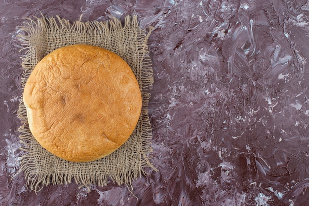 Foto gratuita una pagnotta di pane tondo con una crosta su una tela di sacco.