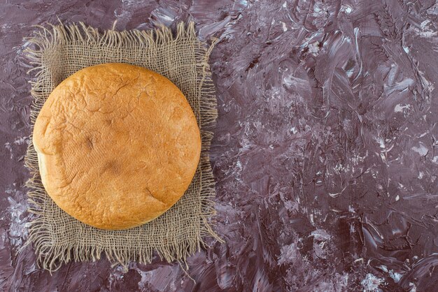 A loaf of round bread with a crust on a sackcloth . 