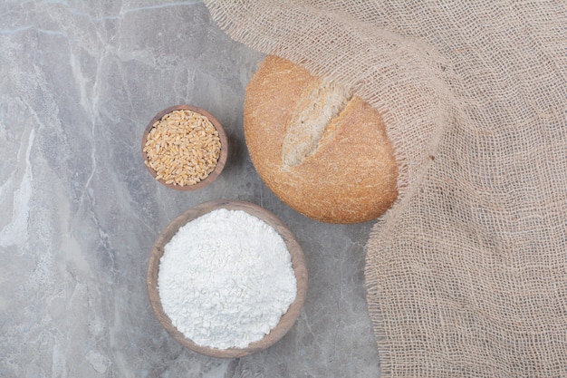 A loaf of white bread with oat grains and flour on marble surface