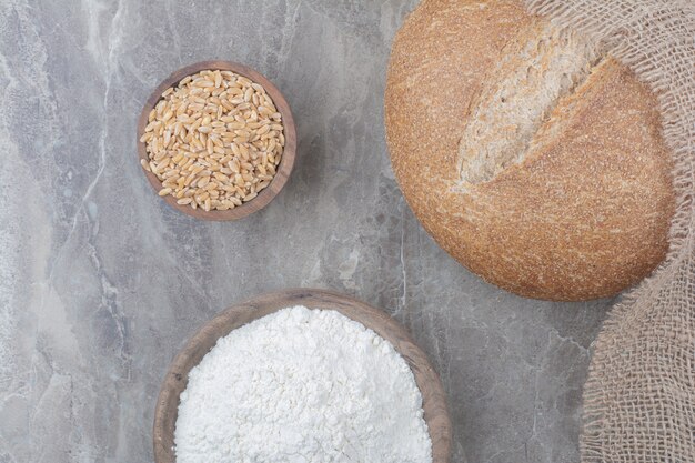 Буханка белого хлеба с овсяными зернами и мукой на мраморной поверхности