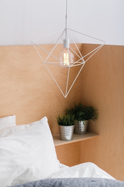 Loft style geometric white ceiling lamp with light wooden background and an edison bulb. 